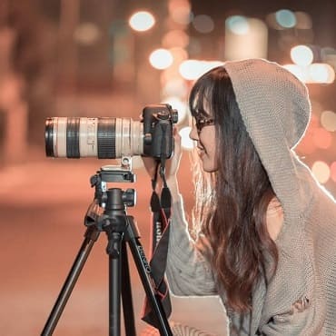 Une femme regarde vers la gauche dans un appareil photo professionnel fixé sur un trepied